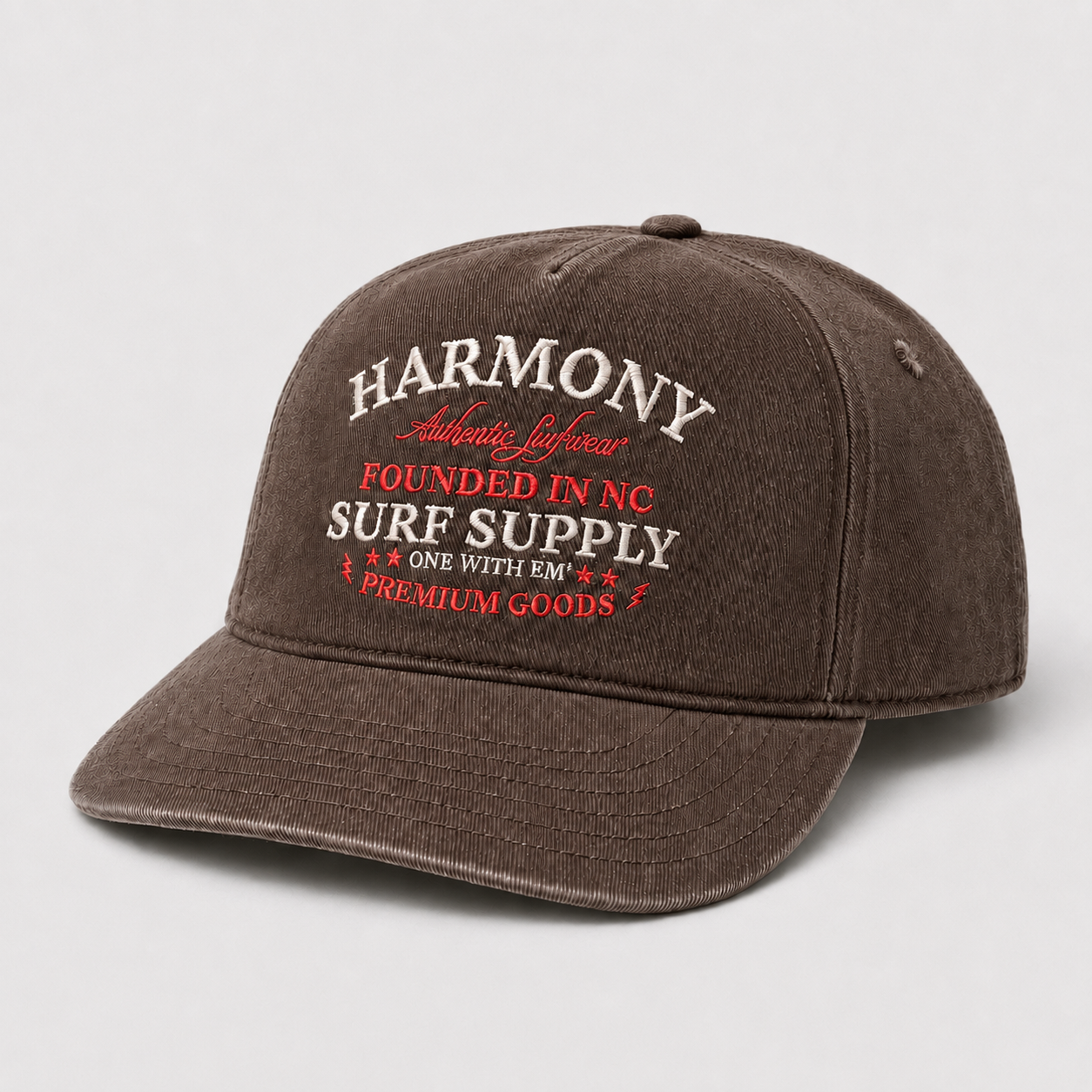 A dark brown washed cotton baseball cap with embroidered text on the front reading 'HARMONY SURF SUPPLY' in white and red, shown on a light gray background.