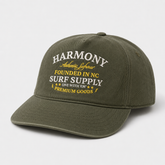 An olive green baseball cap with embroidered text on the front reading 'HARMONY Authentic Lifestyle FOUNDED IN NC SURF SUPPLY ONE WITH EM PREMIUM GOODS' in white and yellow, shown on a light gray background.