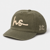 An olive green cotton baseball cap with a curved brim, featuring a glittery beige embroidered 'hs' logo on the front and 'One Rich Life Throug' in white script on the side, set against a light gray background.