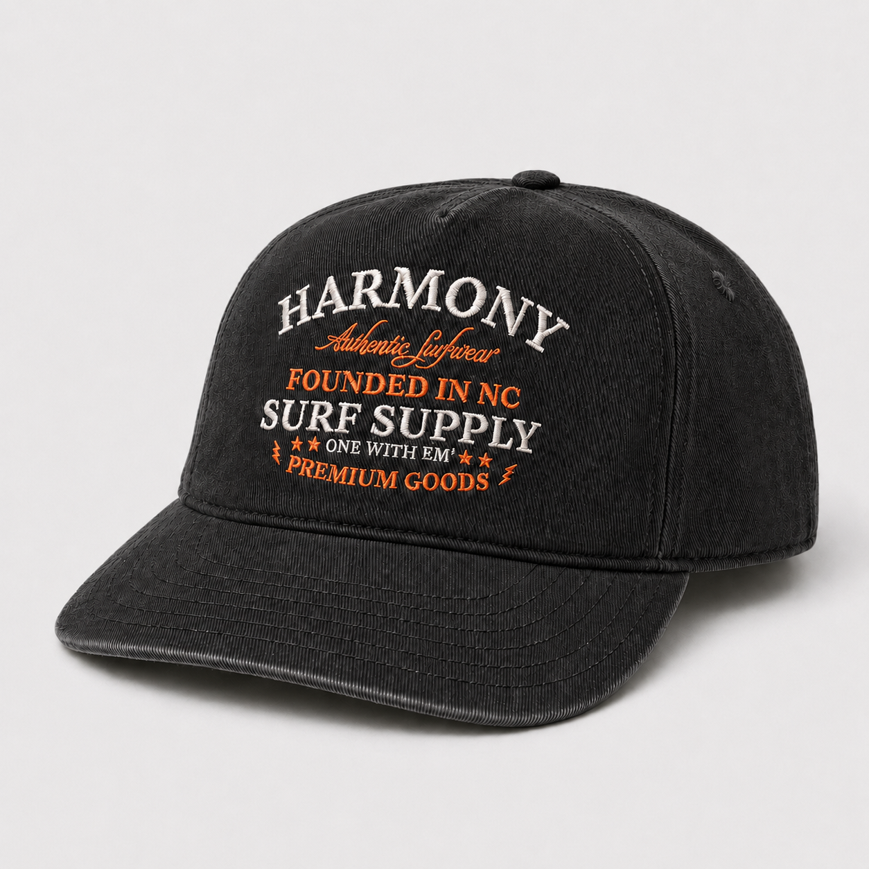 A black washed baseball cap with embroidered text on the front reading 'HARMONY Authentic Lifestyle FOUNDED IN NC SURF SUPPLY ONE WITH EM PREMIUM GOODS' in white and orange, shown on a light gray background.